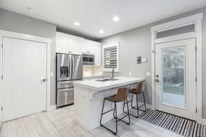 Kitchen featuring appliances with stainless steel finishes, sink, white cabinets, a kitchen bar, and kitchen peninsula