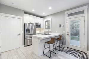 Kitchen featuring appliances with stainless steel finishes, a kitchen breakfast bar, a sink, and light wood finished floors