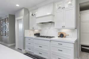 Kitchen with stainless steel gas stovetop, white cabinetry, premium range hood, and backsplash