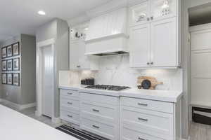 Kitchen featuring stainless steel gas cooktop, white cabinetry, light countertops, and custom range hood