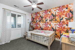 Carpeted bedroom with baseboards, visible vents, an accent wall, wallpapered walls, and a ceiling fan