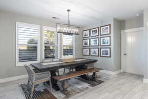 Dining area featuring light wood finished floors, baseboards, visible vents, and a chandelier