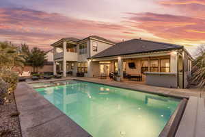 Pool at dusk featuring an outdoor living space, a patio, ceiling fan, and a bar