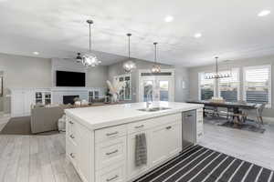 Kitchen with sink, light hardwood / wood-style flooring, hanging light fixtures, an island with sink, and white cabinets