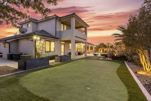 Back house at dusk with a balcony, outdoor lounge area, central AC, and a patio area