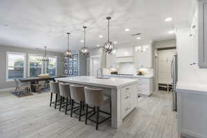 Kitchen featuring premium range hood, sink, white cabinetry, decorative light fixtures, and a center island with sink