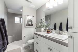 Bathroom featuring walk in shower, visible vents, toilet, and vanity