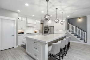 Kitchen with sink, appliances with stainless steel finishes, white cabinetry, an island with sink, and custom range hood