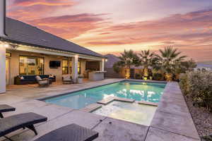 Pool at dusk with an outdoor kitchen, outdoor lounge area, an in ground hot tub, ceiling fan, and a patio