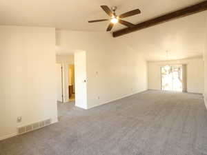 Carpeted spare room with vaulted ceiling with beams and ceiling fan with notable chandelier