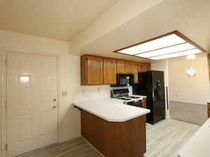 Kitchen with a skylight, light hardwood / wood-style flooring, hanging light fixtures, kitchen peninsula, and black appliances