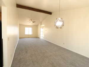 Carpeted spare room featuring ceiling fan with notable chandelier and vaulted ceiling with beams