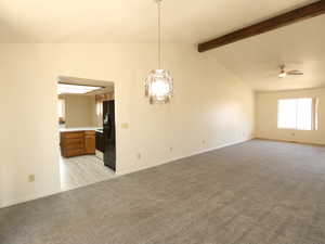 Carpeted empty room featuring ceiling fan and vaulted ceiling with beams