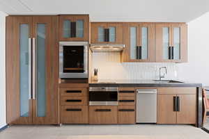 Kitchen featuring oven, wall oven, tasteful backsplash, sink, and wall chimney exhaust hood