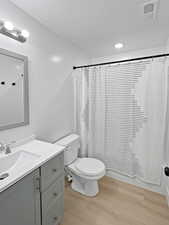 Full bathroom with wood-type flooring, vanity, toilet, shower / bathtub combination with curtain, and a textured ceiling