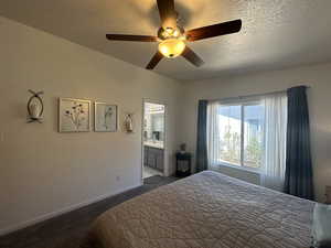 Bedroom with ceiling fan, ensuite bath, dark carpet, and a textured ceiling