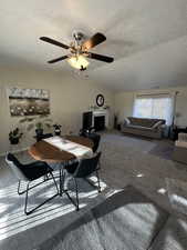 Carpeted dining area featuring ceiling fan, lofted ceiling, and a textured ceiling