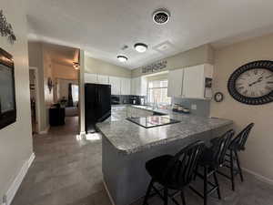 Kitchen with kitchen peninsula, lofted ceiling, white cabinets, a kitchen breakfast bar, and black appliances