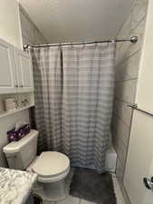 Full bathroom featuring vanity, a textured ceiling, tile patterned floors, toilet, and shower / bath combo with shower curtain