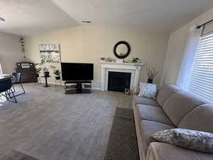 Living room featuring a tiled fireplace, vaulted ceiling, carpet flooring, and a textured ceiling