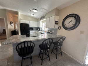 Kitchen featuring sink, a breakfast bar area, white cabinetry, kitchen peninsula, and black appliances