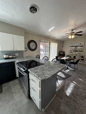 Kitchen featuring stainless steel range with electric cooktop, white cabinetry, light stone counters, kitchen peninsula, and black dishwasher