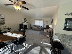 Dining space with lofted ceiling, ceiling fan, a textured ceiling, and carpet flooring