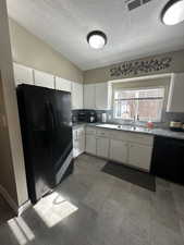 Kitchen with vaulted ceiling, sink, white cabinets, black appliances, and a textured ceiling