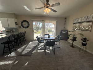 Dining space featuring dark colored carpet, ceiling fan, and a textured ceiling