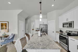 Kitchen with stainless steel appliances, an island with sink, hanging light fixtures, and white cabinetry