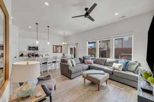 Living room with ceiling fan with notable chandelier and light wood-type flooring