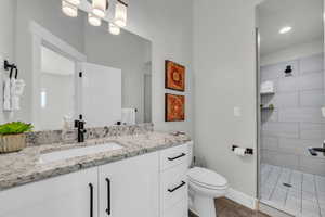 Bathroom featuring hardwood / wood-style floors, vanity, a tile shower, and toilet