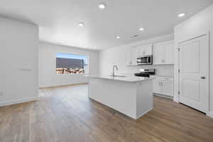 Kitchen with sink, a center island with sink, white cabinets, and appliances with stainless steel finishes