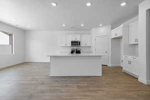 Kitchen featuring stainless steel appliances, white cabinetry, an island with sink, and light hardwood / wood-style flooring