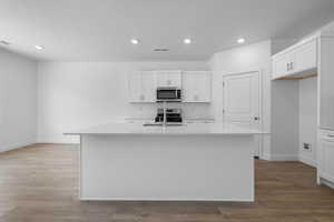 Kitchen featuring wood-type flooring, appliances with stainless steel finishes, a center island with sink, and white cabinets