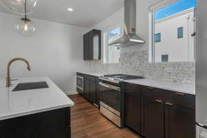 Kitchen featuring appliances with stainless steel finishes, sink, hanging light fixtures, dark wood-type flooring, and wall chimney exhaust hood