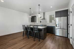 Kitchen with decorative light fixtures, dark hardwood / wood-style flooring, decorative backsplash, stainless steel appliances, and wall chimney range hood