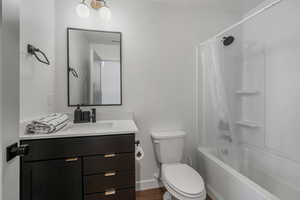 Full bathroom with hardwood / wood-style flooring, shower / tub combo with curtain, vanity, and toilet