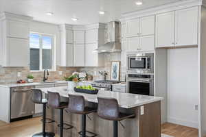 Kitchen with wall chimney exhaust hood, white cabinetry, stainless steel appliances, and sink