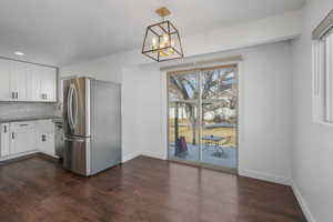 Kitchen featuring dark wood-type flooring, decorative light fixtures, white cabinets, stainless steel appliances, and backsplash