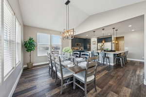 Dining room featuring vaulted ceiling, dark wood-type flooring, sink, and an inviting chandelier