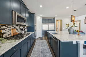 Kitchen featuring sink, hanging light fixtures, stainless steel appliances, a center island with sink, and dark hardwood / wood-style flooring