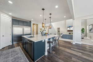 Kitchen featuring sink, light stone counters, a center island with sink, appliances with stainless steel finishes, and pendant lighting