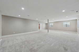 Basement with light colored carpet and a textured ceiling