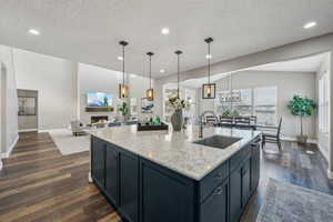 Kitchen featuring decorative light fixtures, sink, a kitchen island with sink, light stone counters, and dark wood-type flooring