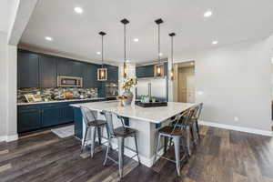 Kitchen with a breakfast bar area, hanging light fixtures, dark hardwood / wood-style floors, stainless steel appliances, and a kitchen island with sink