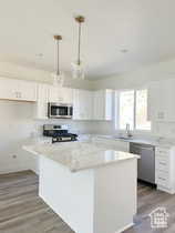 Kitchen with sink, white cabinetry, wood-type flooring, hanging light fixtures, and appliances with stainless steel finishes