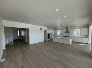 Kitchen with sink, white cabinetry, dark hardwood / wood-style floors, an island with sink, and wall chimney exhaust hood