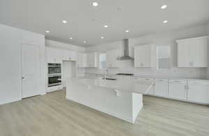 Kitchen with a kitchen island with sink, white cabinets, light countertops, appliances with stainless steel finishes, and wall chimney exhaust hood