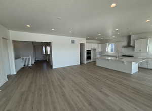 Kitchen with white cabinets, sink, a kitchen island with sink, and wall chimney range hood